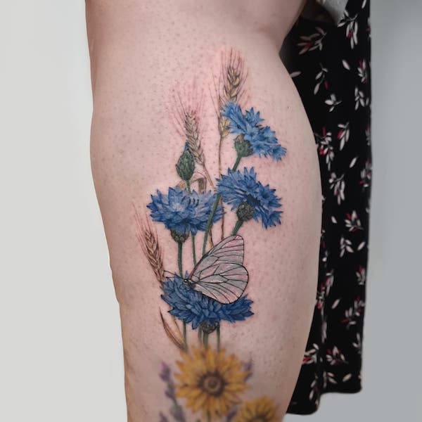 Leg tattoo of a butterfly perched cornflower