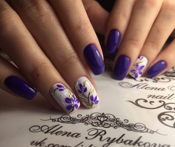 Художній дизайн Nail Art.  Захистіть цвяхи цим дивним синювато-пурпурним і білим дизайнерським дизайном нігтів з висіченими квітами.  Налаштування золота багато чого додає до цього твору мистецтва.